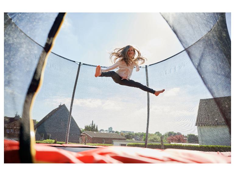 Glückliches Mädchen springt hoch auf einem Trampolin unter freiem Himmel.