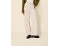 Frau in grüner Strickjacke, heller Hose und schwarzen Loafern.