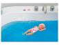 Babypuppe schwimmt in blauem Wasser in einer Badewanne, trägt einen rosa Badeanzug.