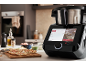 Smarte Küchenmaschine mit Touchscreen, der ein Flammkuchen-Rezept anzeigt, mit einem fertigen Flammkuchen daneben.