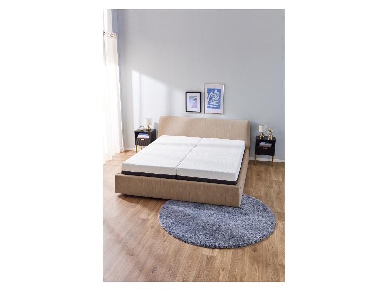 Beiges Bett mit zwei weißen Matratzen in einem Schlafzimmer mit Holzboden und rundem Teppich.
