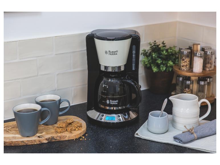 Eine schwarze Russell Hobbs Kaffeemaschine mit zwei grauen Tassen und einem Snack auf einem Holzbrett.