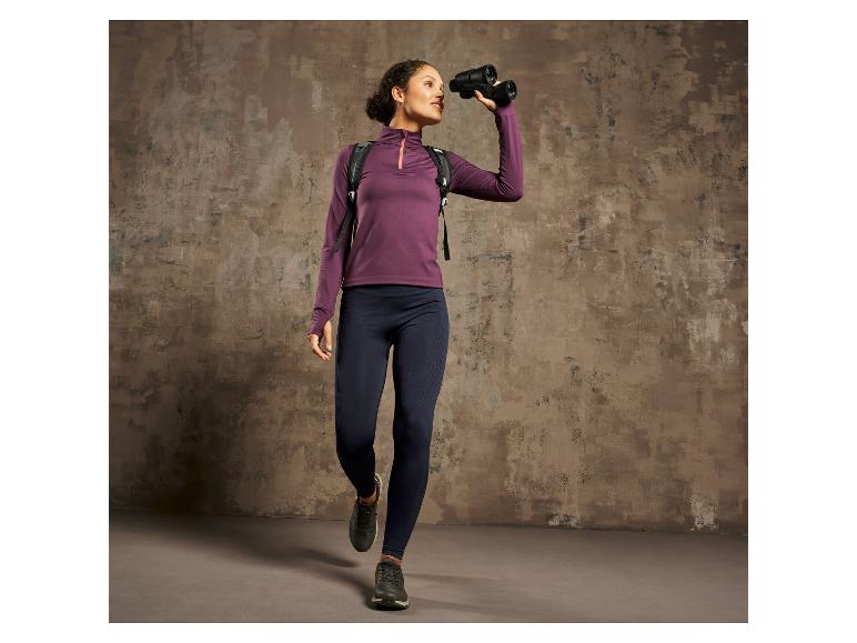 Eine Frau in einem lila Pulli und blauen Leggings schaut durch ein Fernglas.