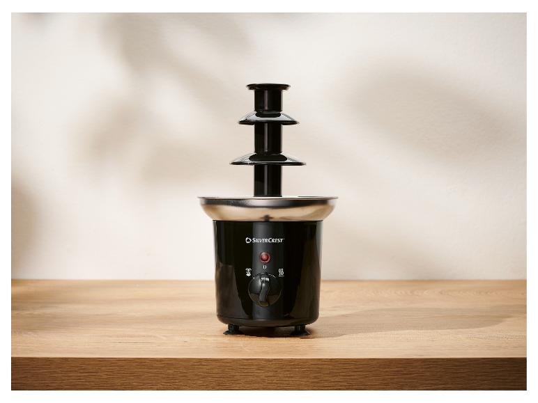 Ein schwarzer dreistufiger Schokoladenbrunnen mit Edelstahlbasis auf einem Holztisch.