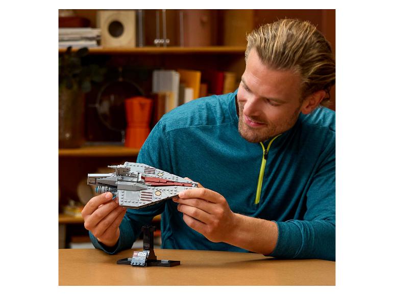 Ein Mann lächelt, während er ein LEGO Star Wars Raumschiff hält.