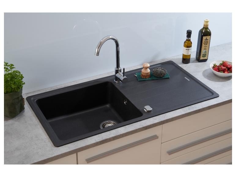 Schwarze Küchenspüle mit Wasserhahn, Schwämmen und Olivenölflaschen auf der Arbeitsplatte.