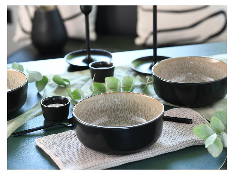 Gedeckter Tisch mit schwarzen und beigen Schalen, Kerzen und einem Eukalyptuszweig.