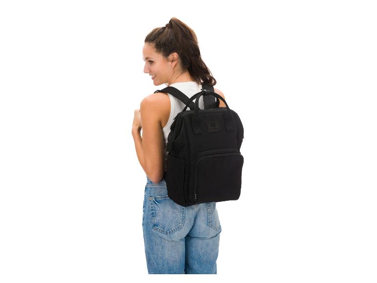 Lächelnde Frau mit schwarzem Rucksack auf dem Rücken, trägt Jeans und ein weißes Top.