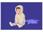 Glückliches Baby in cremefarbener Kapuzen-Fleecejacke und grauen Leggings, sitzt neben einem lila Sternenkissen.