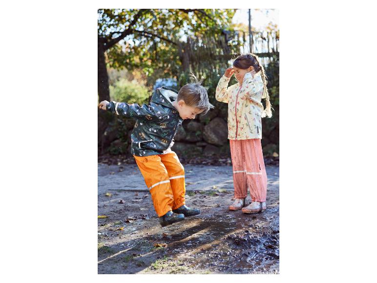 Zwei Kinder in Regenkleidung spielen in einer Pfütze.