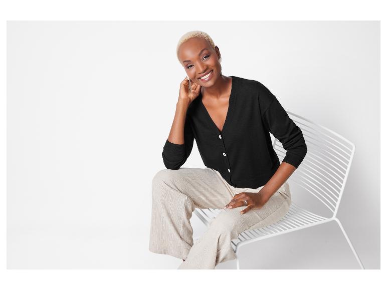 Model trägt einen schwarzen Cardigan und eine hellbeige Hose.