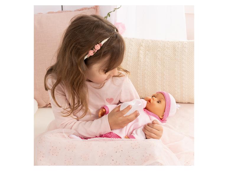 Mädchen füttert eine Puppe mit einer Babyflasche, in Rosa gekleidet.