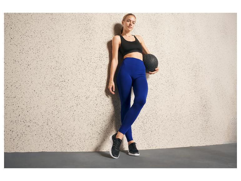 Eine Frau in blauen Leggings und schwarzen Sneakern hält einen Medizinball.