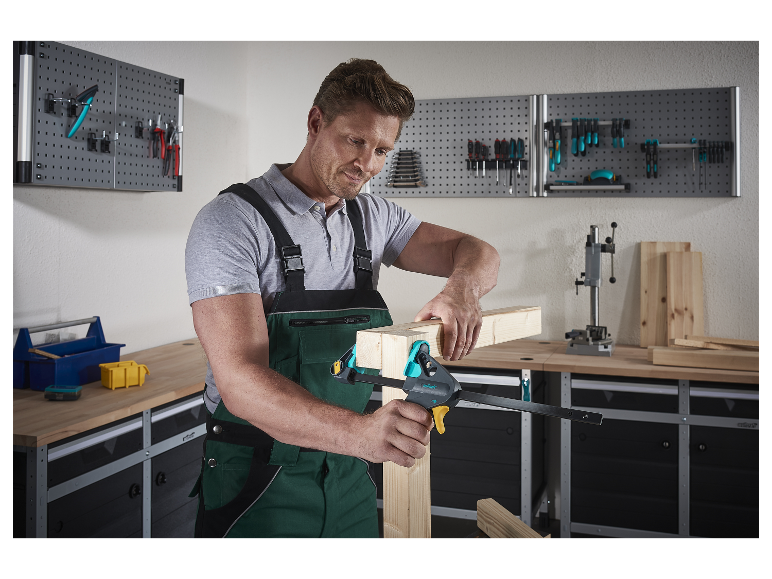 Ein Mann verwendet eine Wolfcraft-Zwinge, um Holzstücke in seiner Werkstatt zu verbinden.