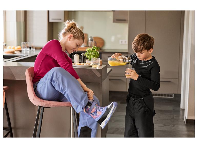 Frau und Kind in der Küche, Kind gießt Saft ein, Frau zieht Stiefel an.