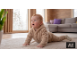 Baby krabbelt auf Teppich in beigem Overall.