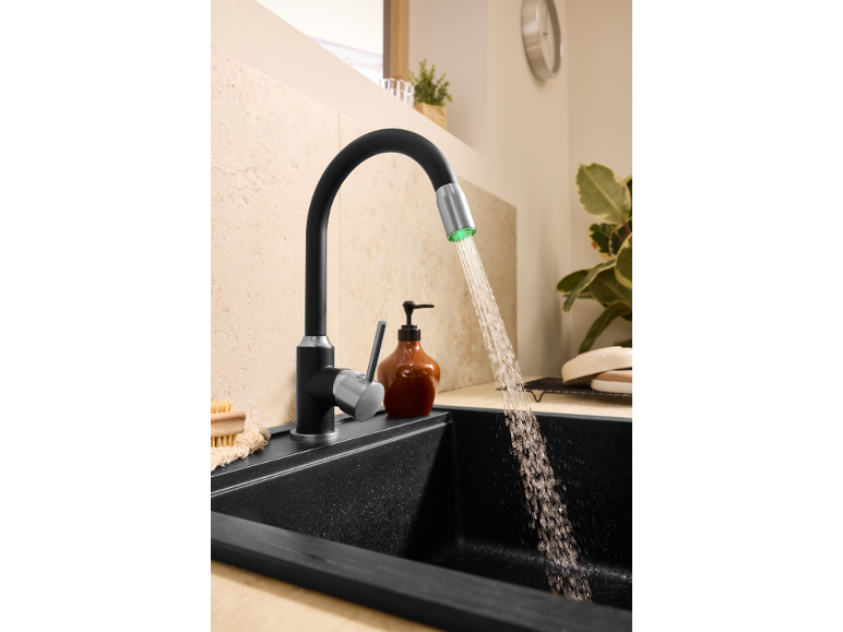 Schwarzer Küchenhahn mit grünem LED-Licht und fließendem Wasser in einer schwarzen Spüle.