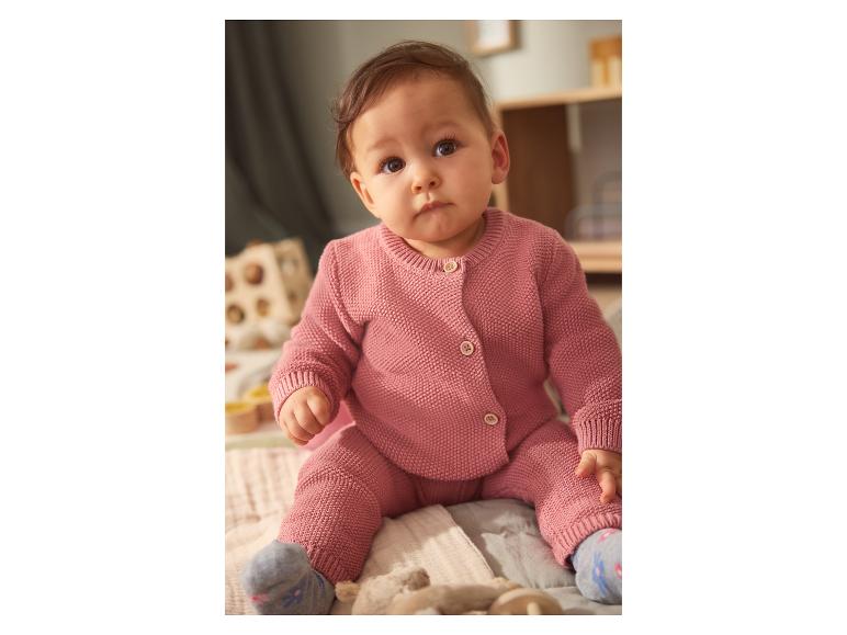 Baby in rosa Strickset, sitzend auf einer weichen Decke.