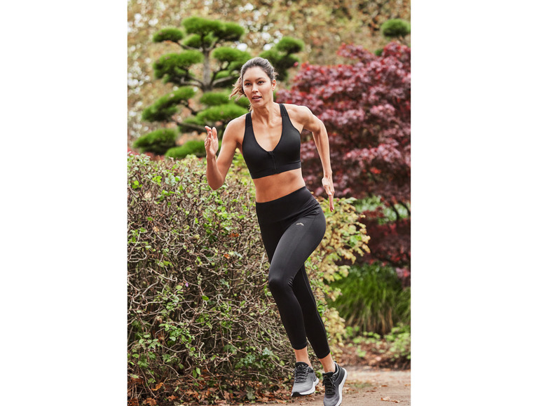 Eine Frau in schwarzem Sport-BH und Leggings joggt durch einen Park.