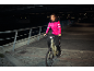 Frau in pinker Jacke und schwarzer Hose auf E-Bike bei Nacht
