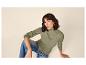 Frau in olivgrünem Rippstrickpullover und blauen Jeans, auf dem Boden sitzend.