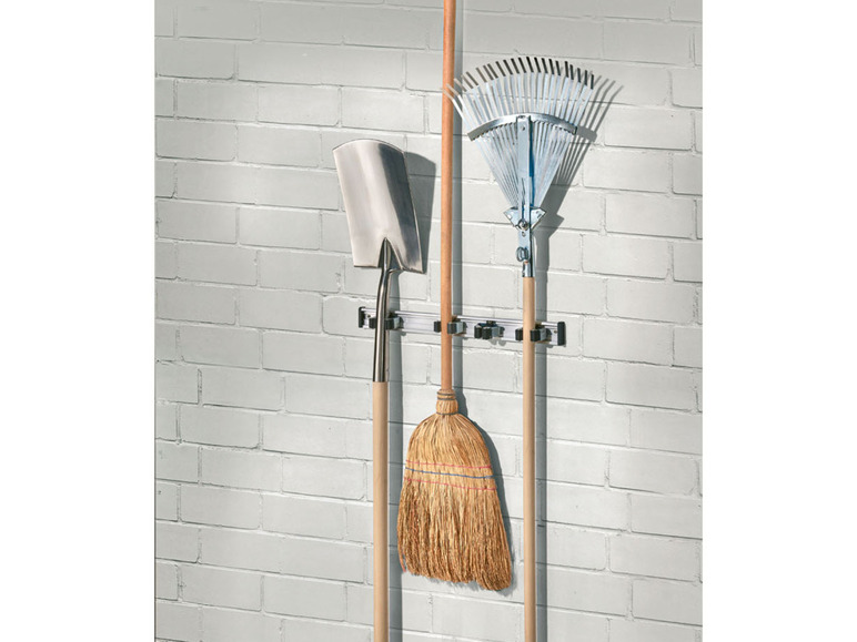 Eine Schaufel, ein Besen und eine Harke hängen an einem Wandhalter.