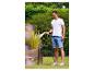 Junger Mann gießt Pflanzen im Garten mit einem Schlauch, trägt ein weißes T-Shirt und Shorts.