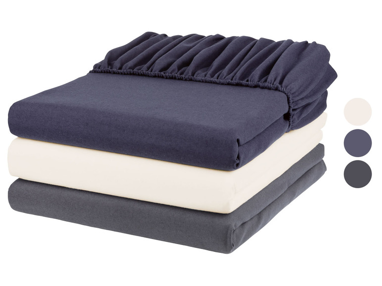 Ein Stapel mit drei Bettlaken in den Farben Dunkelblau, Weiß und Dunkelgrau.