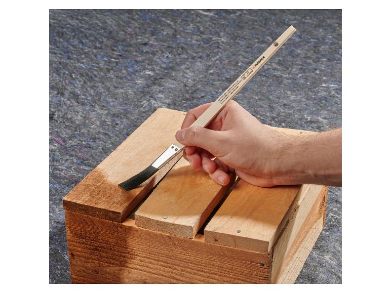 Hand trägt Lack mit Pinsel auf Holzkiste auf, auf grauem Hintergrund.