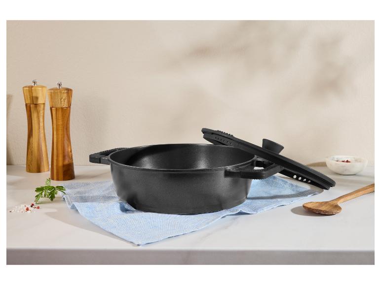 Schwarzer Topf mit Deckel, Salz- und Pfeffermühlen, Holzlöffel und Gewürze auf einer Küchenarbeitsplatte.