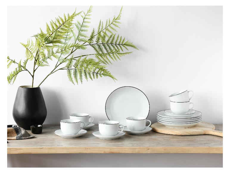 Weiße Kaffeebecher, Teller und Untertassen mit schwarzem Rand auf einem Regal.