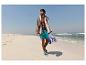 Mann in Badeshorts und mit Handtuch geht am Strand entlang.