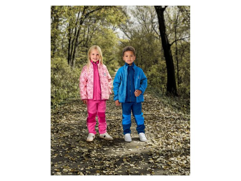 Zwei Kinder in rosa und blauen Regenanzügen auf einem Waldweg.