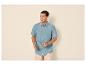 Mann in blauem Kurzarmhemd und beiger Shorts, Sonnenbrille haltend.