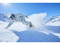Snowboarder im hellblauen Skianzug und Helm fährt eine verschneite Piste hinunter.