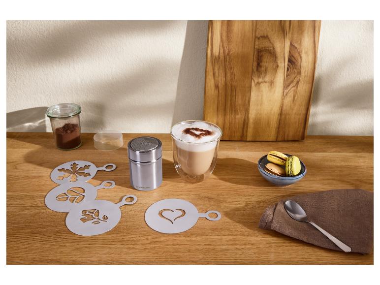 Kaffeeschablonen und Kakao-Streuer mit einem Latte und Macarons auf einem Holztisch.