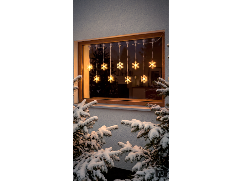 Schneeflocken-Weihnachtsbeleuchtung am Fenster, mit schneebedeckten Tannenbäumen.