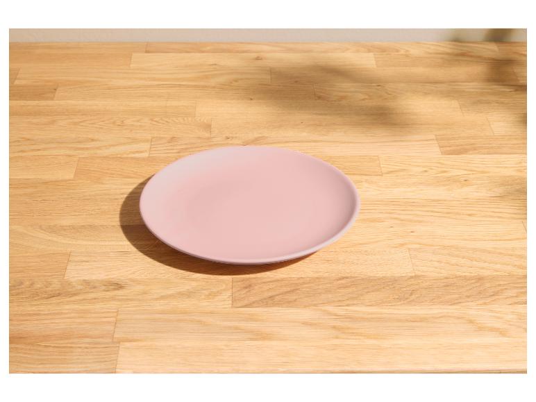 Rosa Teller auf einem hellen Holztisch mit Sonnenlicht und Schatten.