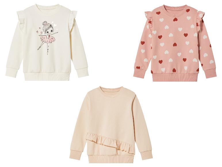 Drei Mädchenpullover mit Rüschen: einer mit Ballerina-Druck, einer mit Herzen und einer einfarbiger.