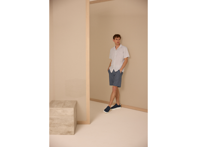 Mann in gestreiftem Hemd, blauen Shorts und Sneakern.