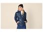 Frau in dunkelblauer Steppjacke, weißem Rollkragenpullover, schwarzer Mütze und blauen Jeans.