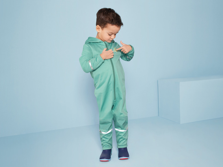 Ein Kind in einem grünen Overall mit reflektierenden Details.