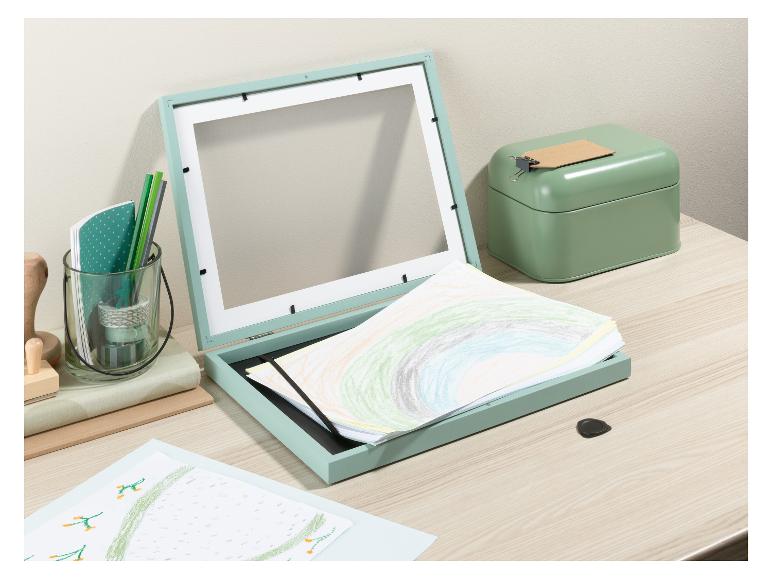 Ein grüner Bilderrahmen mit Zeichnungen und eine grüne Metallbox auf einem Holztisch.