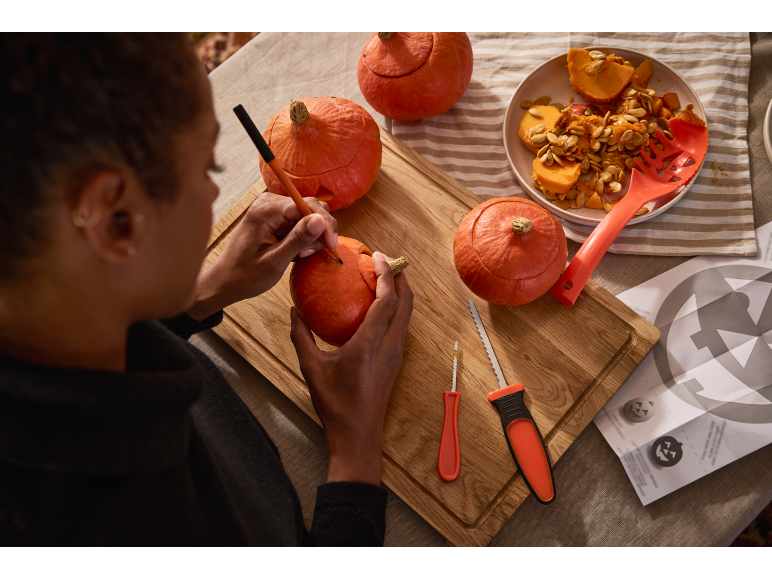 Person schnitzt Halloween-Kürbisse mit Schnitzwerkzeugen und Kernen.