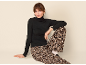 Frau in schwarzem Rollkragenpullover und Hose mit Leopardenmuster sitzt vor hellem Hintergrund.