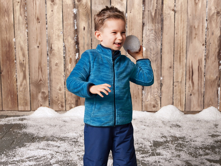 Ein Junge in einer blauen Fleecejacke hält einen Schneeball fest.