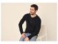 Mann in einem schwarzen Langarm-Henley-Shirt und Jeans, auf einem Stuhl sitzend.