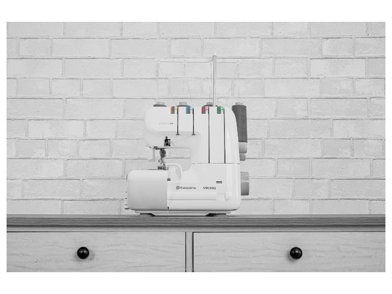 Weiße Overlock-Nähmaschine mit bunten Fäden auf einer Holztheke vor einer Ziegelwand.