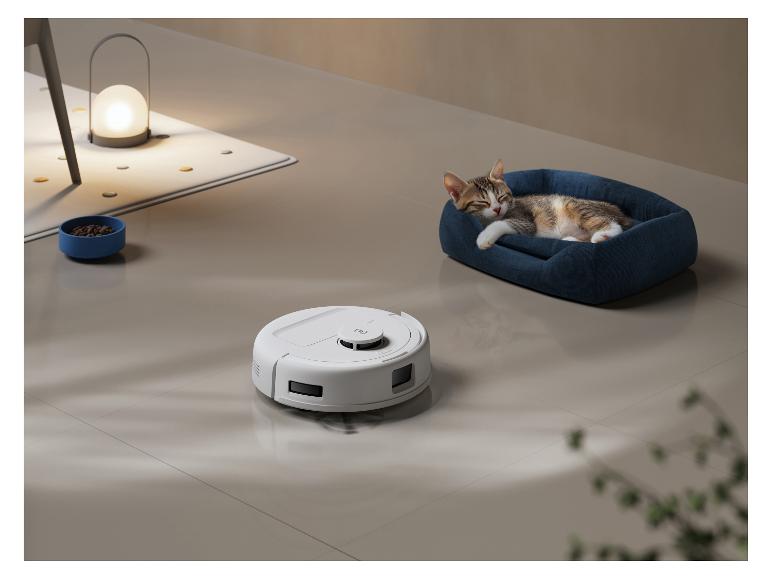 Weißer Saugroboter auf dem Boden mit einer schlafenden Katze in einem blauen Bett.