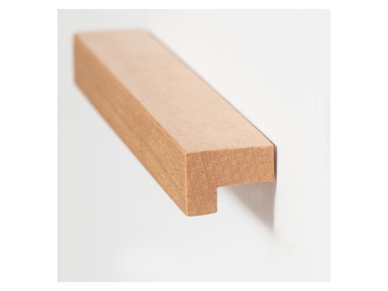 Ein helles Holzstück mit einer Kerbe, an einer weißen Wand montiert.